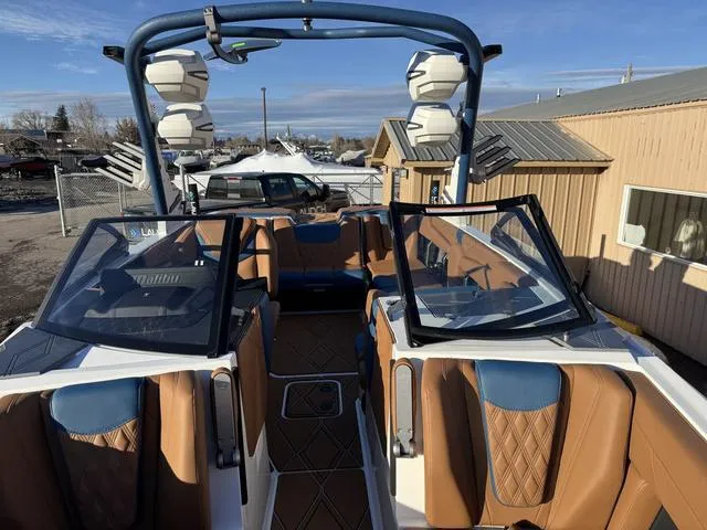 Slide: The Image of 2025 Malibu M230 boat interior with tan and blue seating, open windshield, and tower speakers. - 23