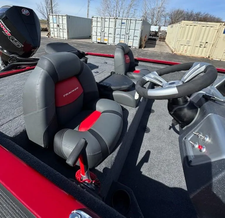 Slide: The Image of 2025 Tracker Savage 215 boat interior with steering wheel and seats, parked near shipping containers. - 7
