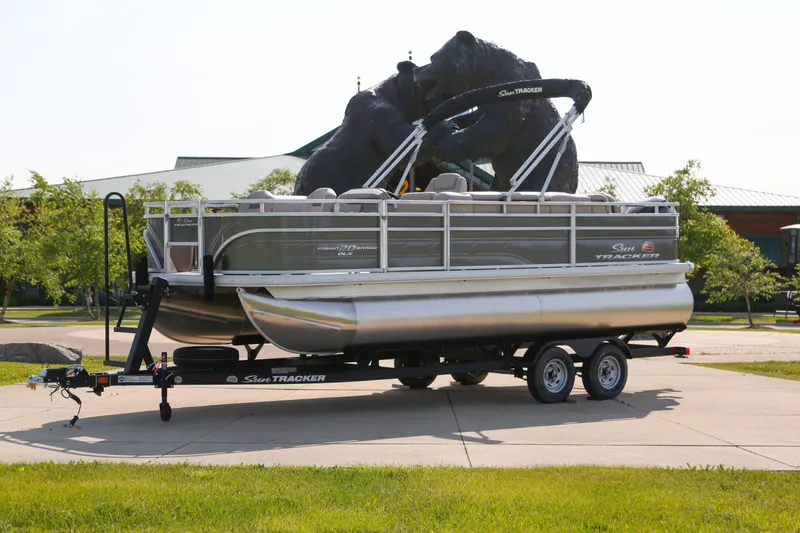 The Image of 2025 Sun Tracker Fishin' Barge 20 DLX pontoon boat on trailer, parked outdoors. - 0