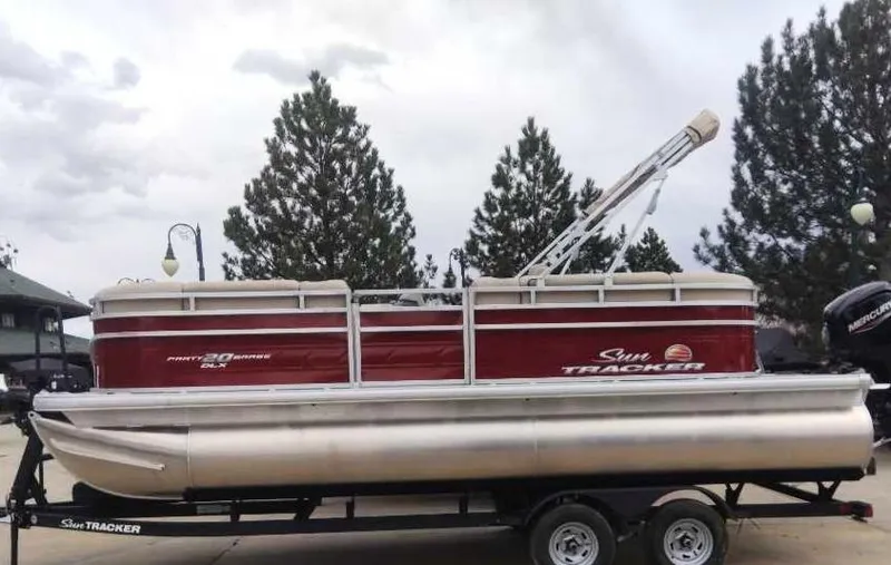 Slide: The Image of 2025 Sun Tracker Party Barge 20 DLX pontoon boat on trailer, parked outdoors. - 2