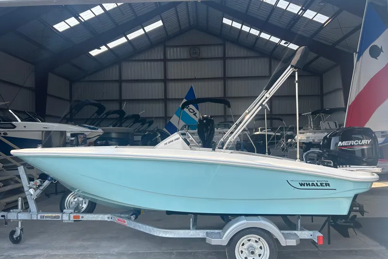 Slide: The Image of 2025 Boston Whaler 130 Super Sport boat in a warehouse, on a trailer. - 2