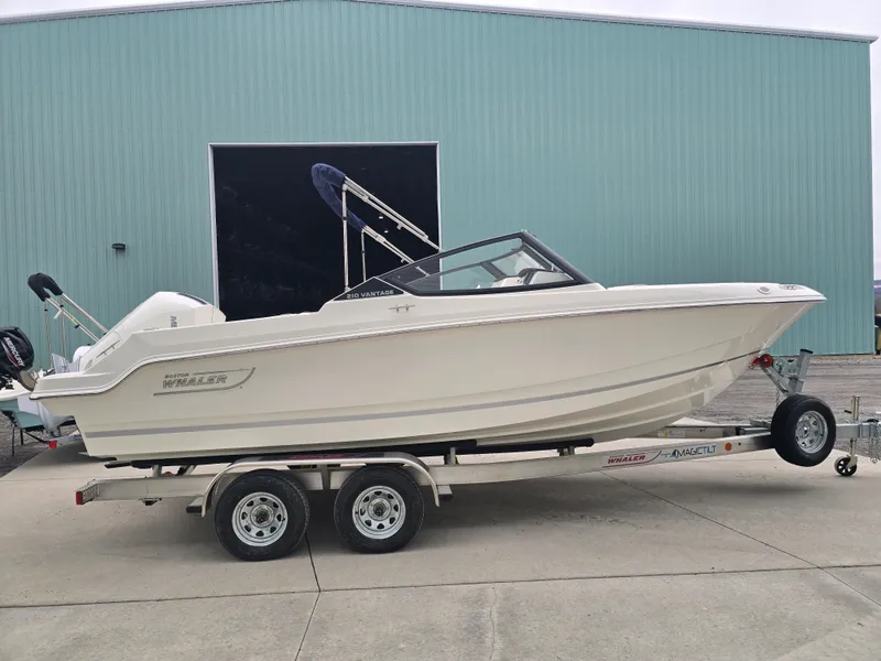 Slide: The Image of 2025 Boston Whaler 210 Vantage boat on trailer, parked outside a large building. - 3