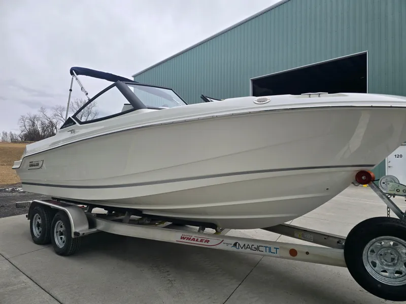 Slide: The Image of 2025 Boston Whaler 210 Vantage boat on trailer near large building. - 30