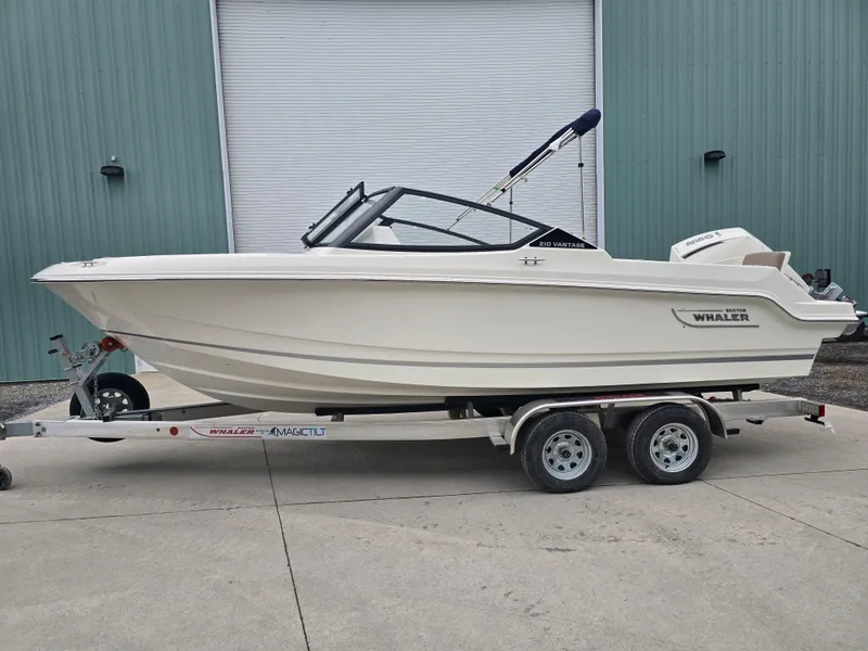 Slide: The Image of 2025 Boston Whaler 210 Vantage boat on trailer, parked outside a warehouse. - 33