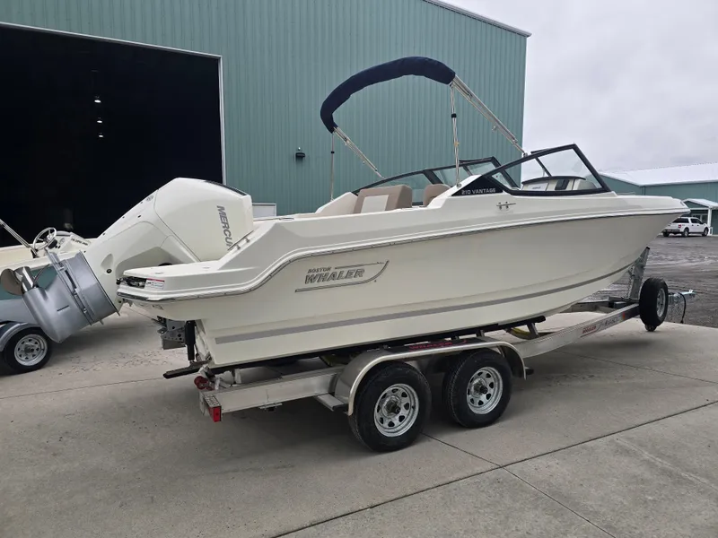 Slide: The Image of 2025 Boston Whaler 210 Vantage boat on trailer near a large warehouse. - 4