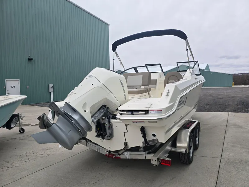 Slide: The Image of 2025 Boston Whaler 210 Vantage boat on trailer, parked outdoors near green building. - 6