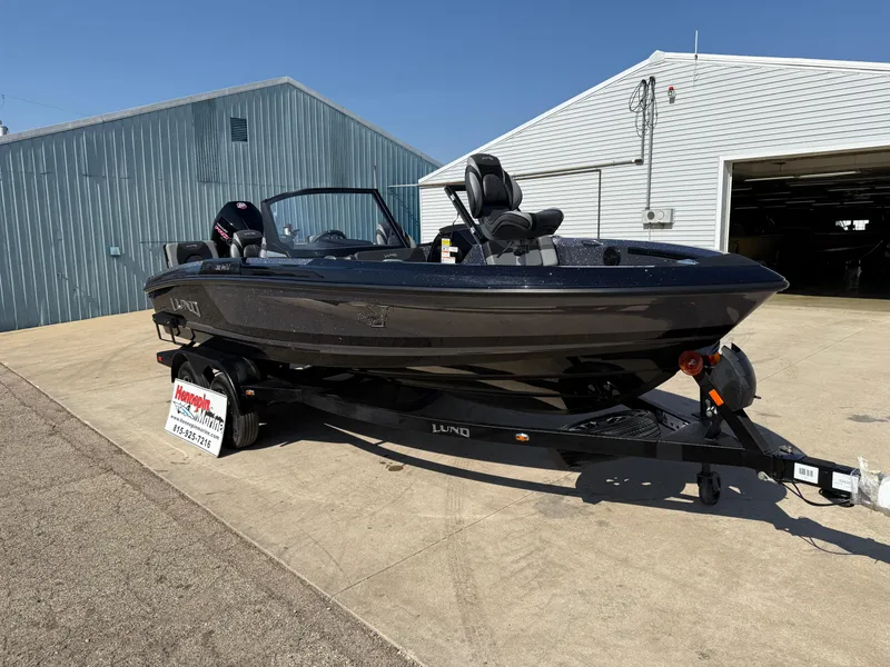 Slide: The Image of 2025 Lund 202 Pro-V GL boat on trailer, parked outside a metal building. - 2