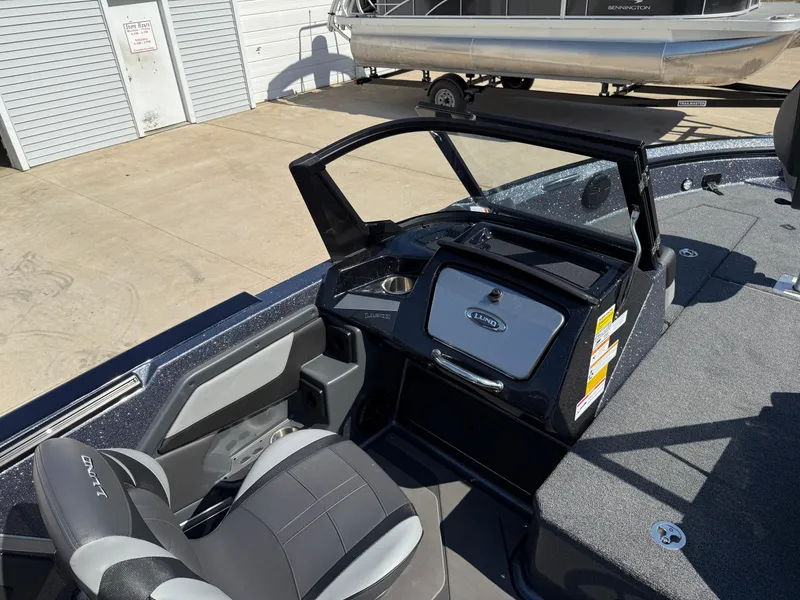 Slide: The Image of 2025 Lund 202 Pro-V GL boat interior with seating and dashboard, parked near a garage. - 21