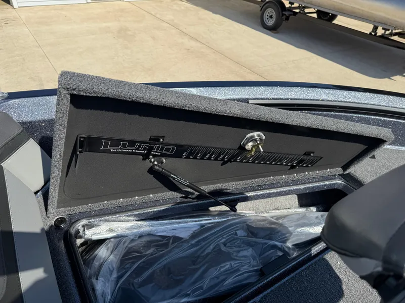 Slide: The Image of 2025 Lund 202 Pro-V GL boat storage compartment with open lid and measuring ruler. - 9