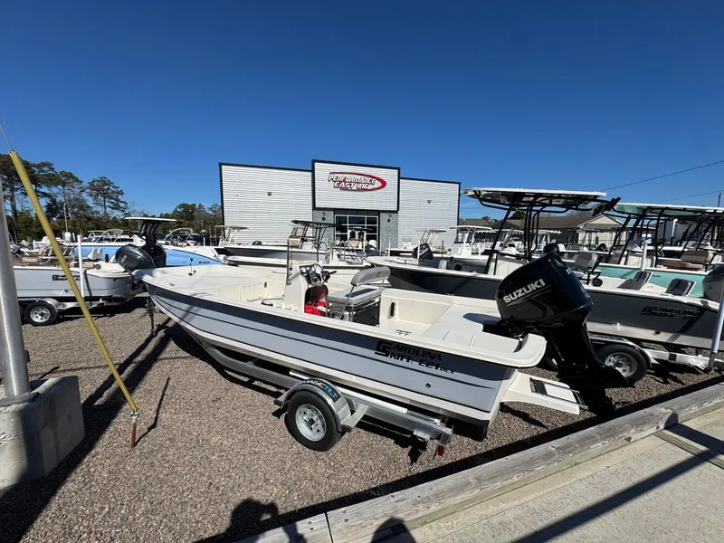 Slide: The Image of 2025 Carolina Skiff E21 DLX CC boat displayed at dealership with Suzuki outboard motor. - 2