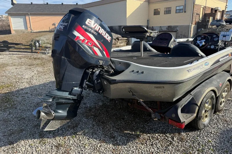Slide: The Image of 2003 Ranger 521DVX boat with Evinrude motor, parked on gravel near buildings. - 2