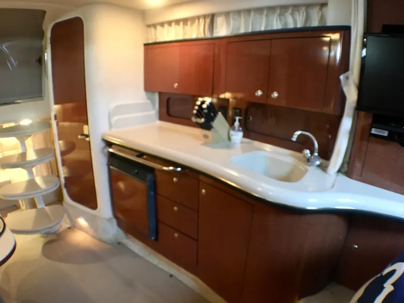 Slide: The Image of Interior of 2002 Sea Ray 320 Sundancer, featuring a compact kitchen with wooden cabinetry. - 13