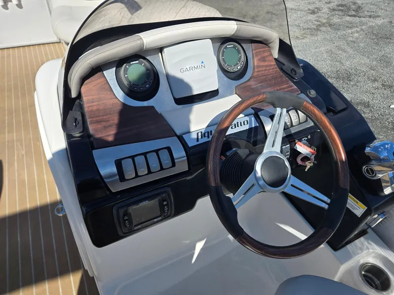 Slide: The Image of 2016 AquaPatio 240 CB boat dashboard with Garmin navigation and wood-accented steering wheel. - 11
