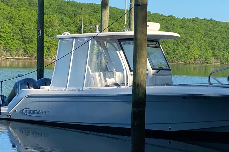 Slide: The Image of 2020 Robalo R272 Center Console boat docked on a serene lake with lush green surroundings. - 32