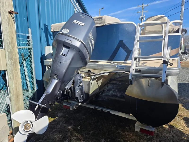 Slide: The Image of 2014 Sweetwater 2086 pontoon boat with outboard motor and ladder, parked near blue building. - 5