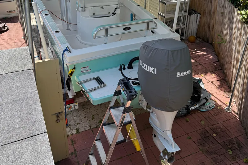 Slide: The Image of 2023 Dusky 252 boat with Suzuki engine cover, parked on brick patio with ladder nearby. - 17