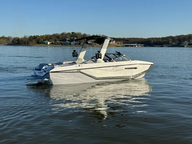 Slide: The Image of 2025 Nautique Super Air Nautique G25 boat on a calm lake under clear skies. - 1