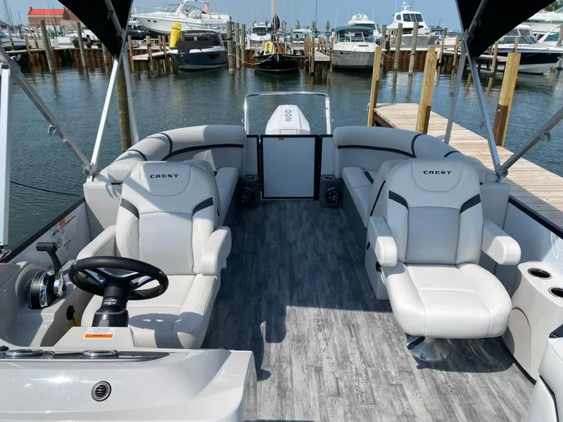 Slide: The Image of 2023 Crest Classic DLX 240 pontoon boat interior with plush seating at a marina. - 3