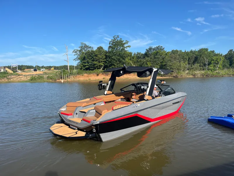 Slide: The Image of 2025 Nautique Super Air Nautique G23 boat on a calm lake under clear blue skies. - 1