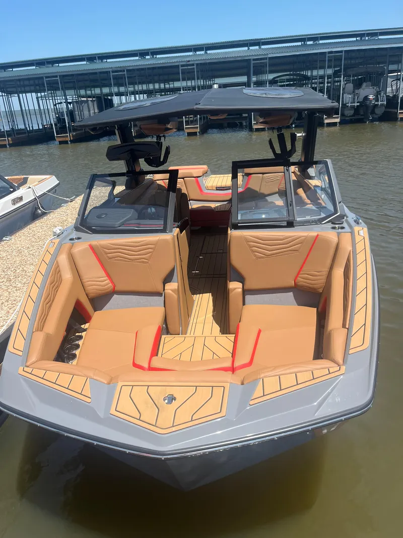 Slide: The Image of 2025 Nautique Super Air Nautique G23 boat with tan seating and sleek design at a marina. - 7