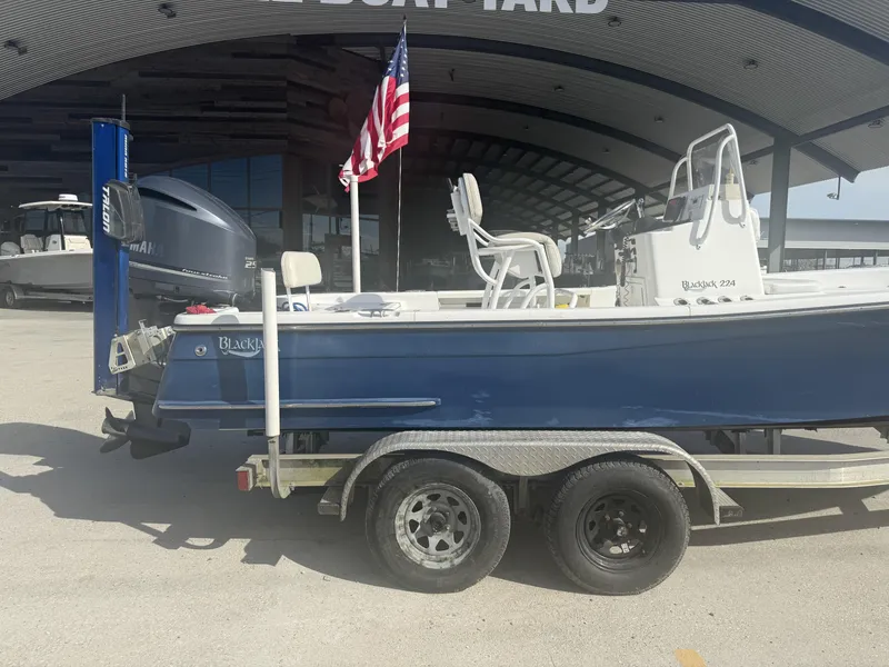 Slide: The Image of Blue 2013 BlackJack 224 boat on trailer, parked outside a boatyard with an American flag. - 14