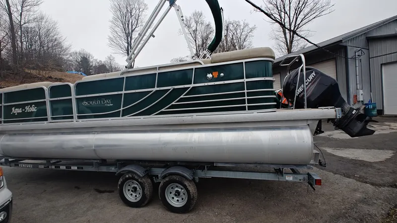 Slide: The Image of 2012 South Bay 722CR pontoon boat on trailer, parked outdoors near a warehouse. - 3