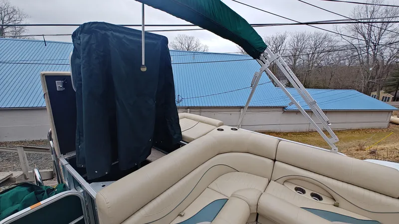 Slide: The Image of 2012 South Bay 722CR pontoon boat with beige seating and green canopy, parked near blue-roofed building. - 6