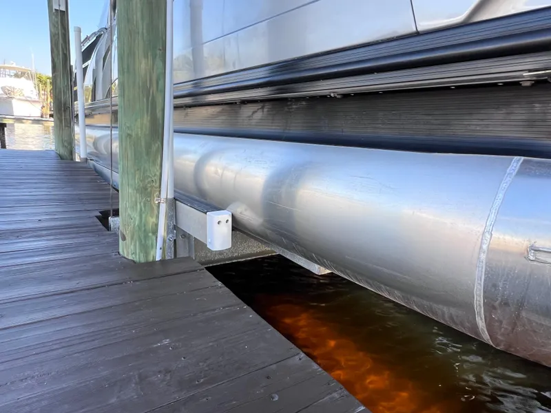 Slide: The Image of 2021 Bennington QX 27 pontoon boat docked, showcasing aluminum pontoons and wooden dock. - 9