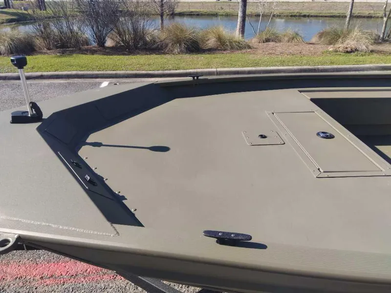 Slide: The Image of 2025 Tracker Grizzly 1654 T Sportsman boat, olive green deck, near a pond. - 7
