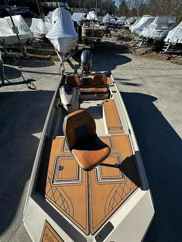 Slide: The Image of 2025 Avid 18 Rogue SC boat with stylish seating and deck design, parked among covered boats. - 5