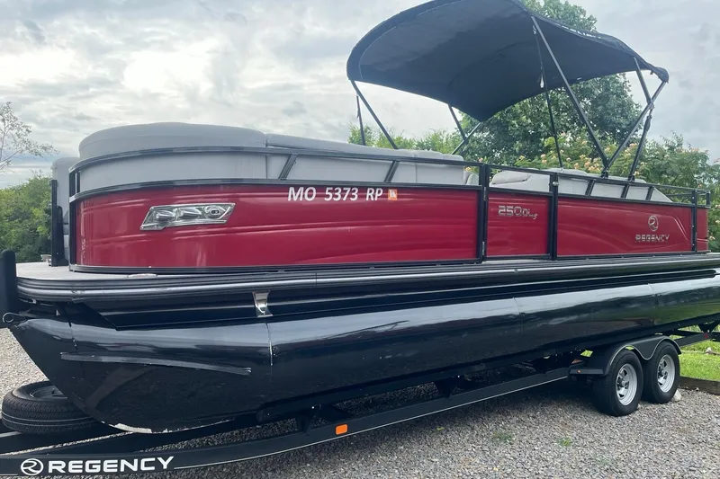 Slide: The Image of 2023 Regency 250DL3 pontoon boat with red exterior on a trailer, featuring a canopy. - 1