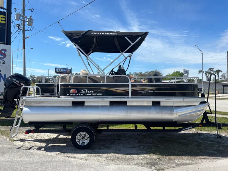 Slide: The Image of 2020 Sun Tracker Bass Buggy 18 DLX pontoon boat on trailer, parked outdoors. - 2