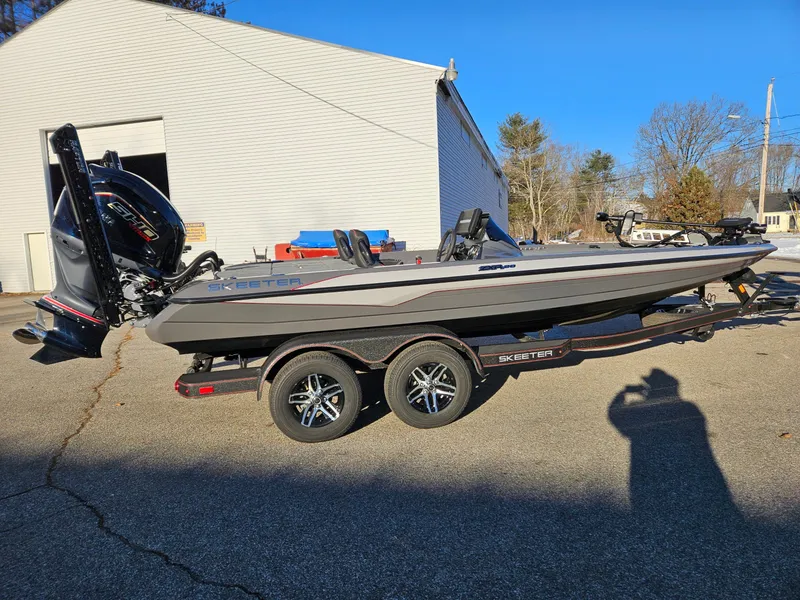 Slide: The Image of 2025 Skeeter ZXR20 boat on trailer, parked outside a building on a sunny day. - 8