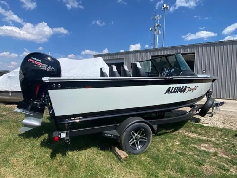 Slide: The Image of 2023 Alumacraft Trophy 185 boat on trailer, parked outdoors under blue sky. - 0