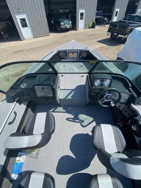 Slide: The Image of 2023 Alumacraft Trophy 185 boat interior with seating and dashboard, parked near a garage. - 10