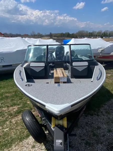 Slide: The Image of 2023 Alumacraft Trophy 185 boat on trailer, outdoors under a partly cloudy sky. - 2