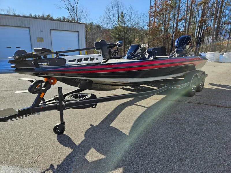 Slide: The Image of 2025 Skeeter ZXR21 boat on trailer, parked outdoors, with trees and building in background. - 3