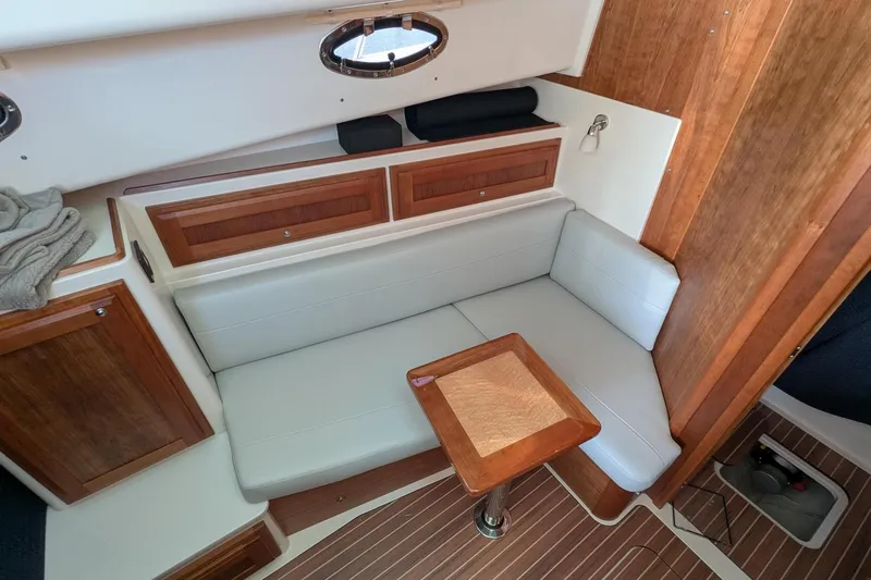 Slide: The Image of 2024 Back Cove 39O interior with wooden accents, white seating, and compact table. - 33