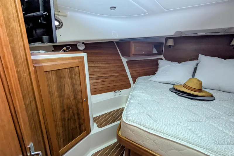 Slide: The Image of 2024 Back Cove 39O cabin interior with wooden finish, bed, and hat on mattress. - 36