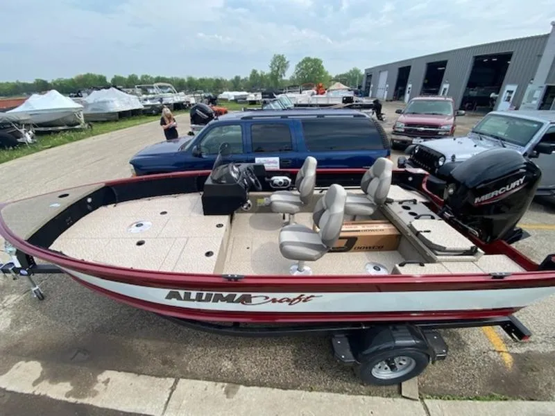 Slide: The Image of 2022 Alumacraft Competitor 165 CS fishing boat on trailer, parked near vehicles. - 2