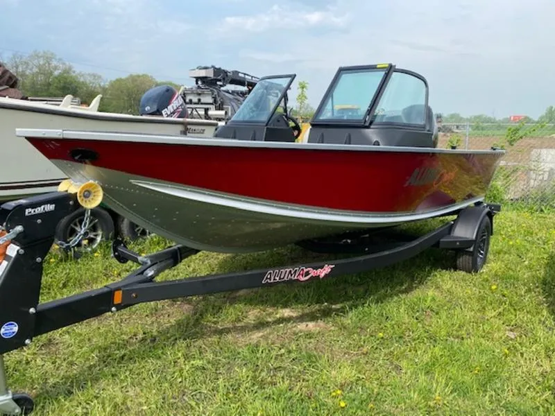 Slide: The Image of 2022 Alumacraft Voyageur 175 Sport boat on trailer, red exterior, parked on grass. - 0