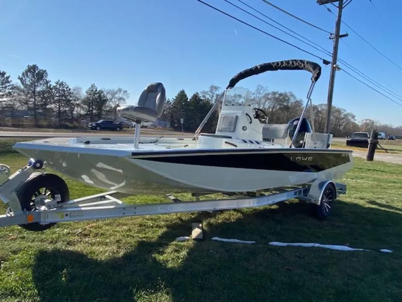 Slide: The Image of 2023 Lowe Bay20 boat on trailer, parked on grass, with trees and power lines in background. - 7