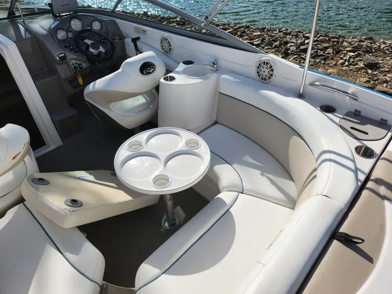 Slide: The Image of 2007 Rinker 246 Captiva Cuddy boat interior with seating and table, near rocky shoreline. - 11