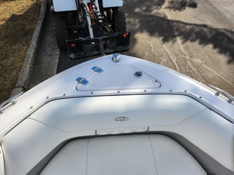 Slide: The Image of 2021 Regal LS2 boat bow with white seating, parked near a tractor on a paved road. - 21