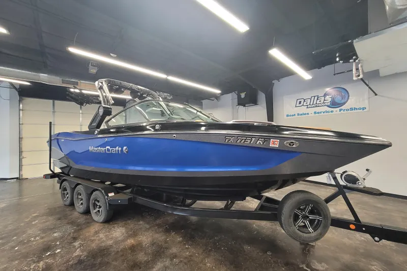 The Image of 2022 MasterCraft X26 boat in showroom, blue and black design, on trailer. - 0