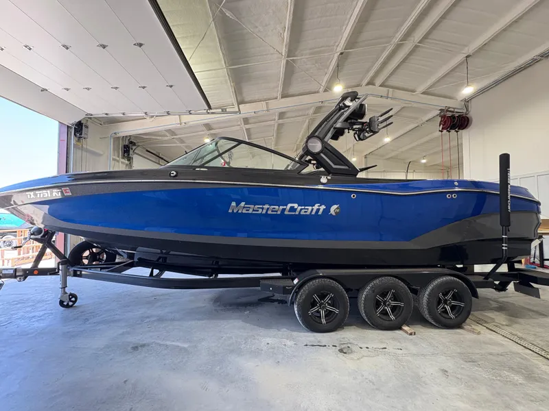 Slide: The Image of 2022 MasterCraft X26 boat in a showroom, blue exterior, on a trailer. - 2