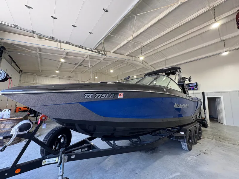 Slide: The Image of 2022 MasterCraft X26 boat in showroom, blue and black exterior, on trailer. - 3