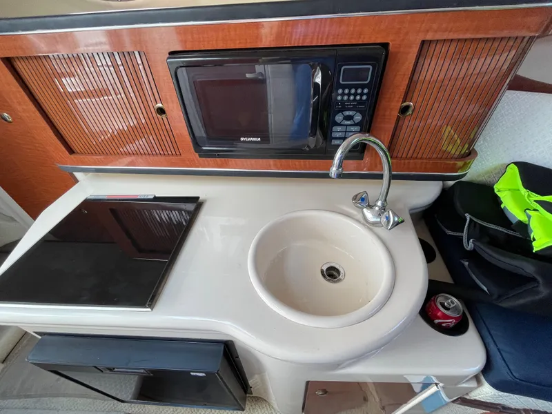 Slide: The Image of 2004 Sea Ray 260 Sundancer kitchenette with microwave, sink, and stove. - 10