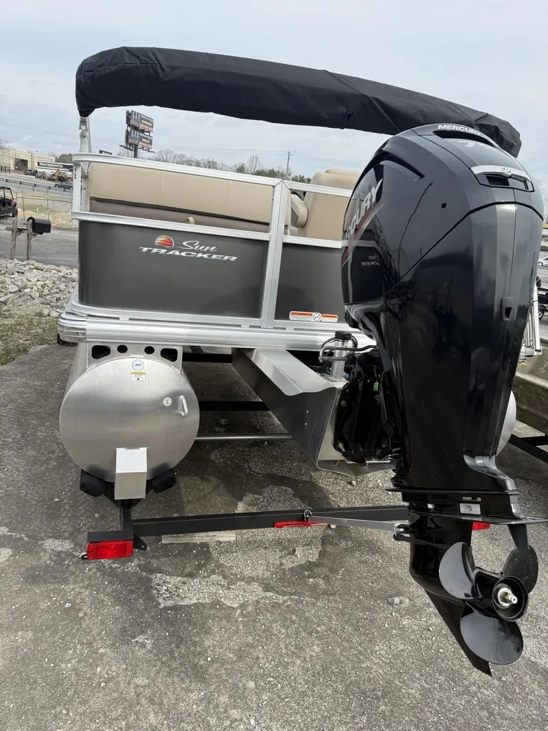 Slide: The Image of 2025 Sun Tracker Party Barge 18 DLX with outboard motor, docked on concrete surface. - 2