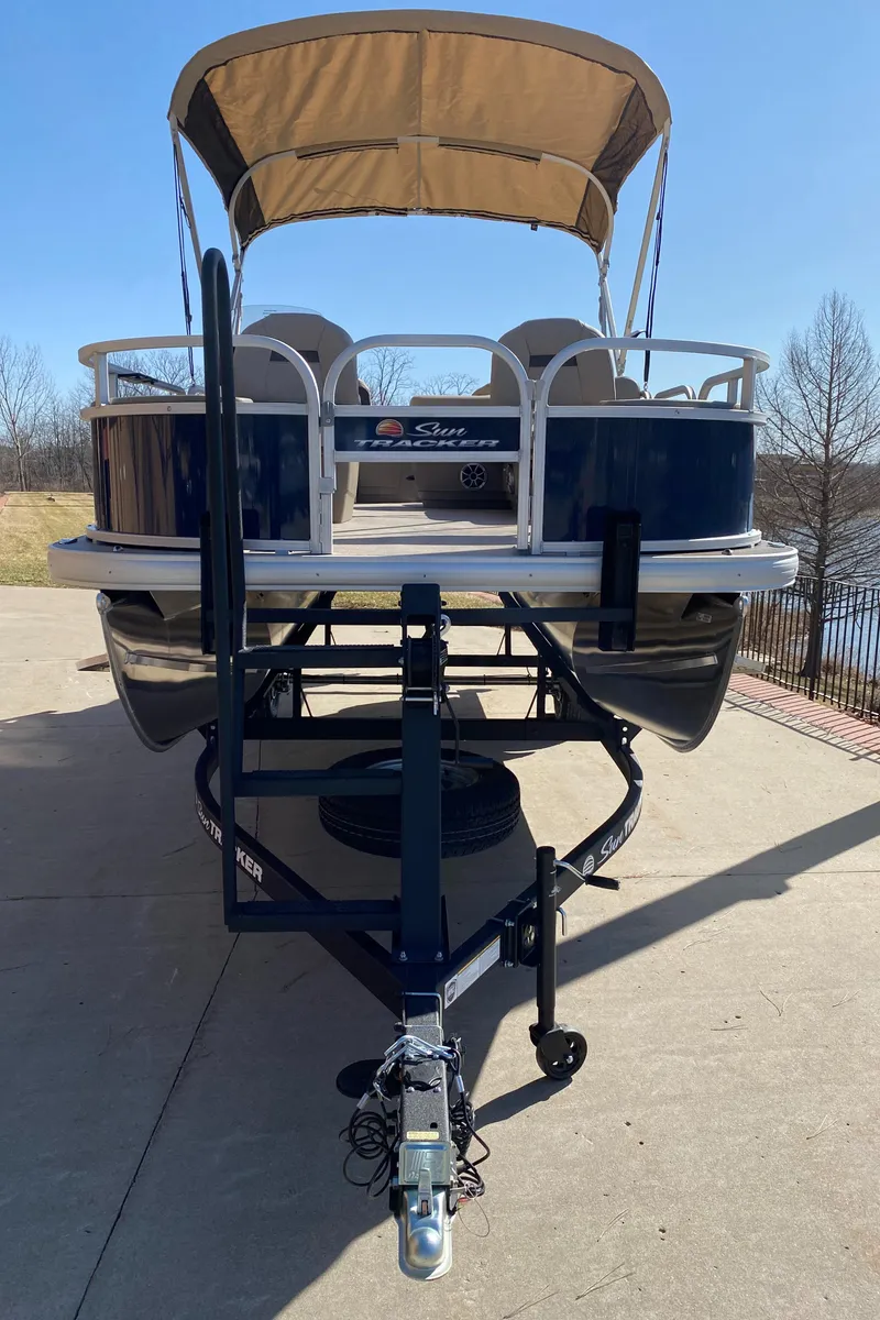Slide: The Image of 2025 Sun Tracker Bass Buggy 18 DLX pontoon boat on trailer, parked outdoors. - 2